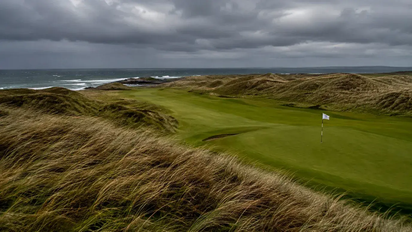 Exposed links golf course with rough grass bending in strong coastal wind