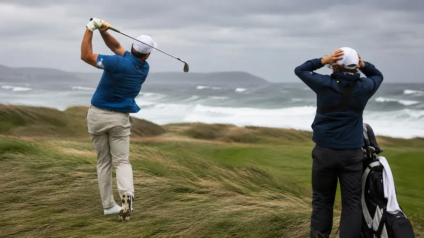 Golfer bracing against strong coastal wind on an exposed links course